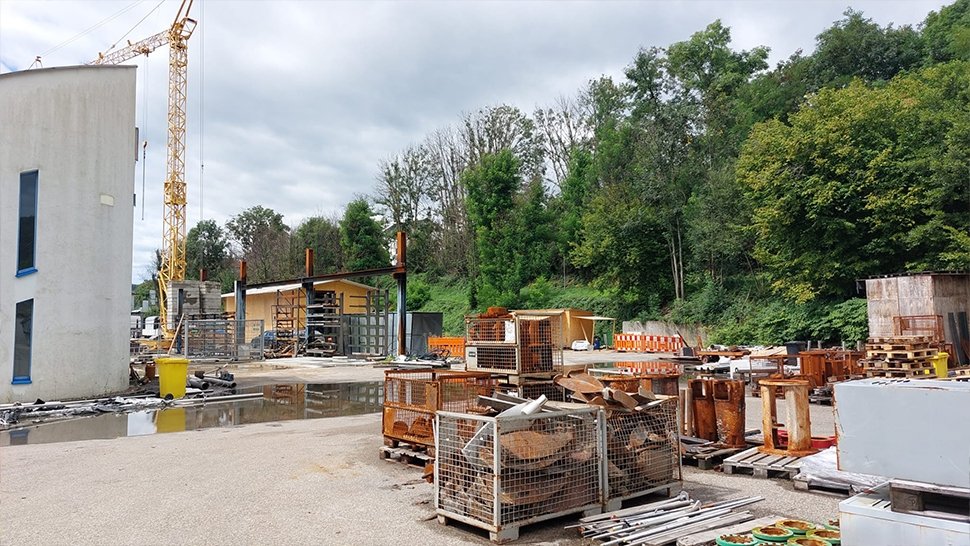 Noch prägt der Baukran das Bild der neuen Fertigungsstätte. Bis zur Fertigstellung wird in einer provisorischen Halle auf dem Gelände (im Hintergrund) und an einem weiteren Standort gefertigt. Im Vordergrund das vom Brand verschonte Treppenhaus.